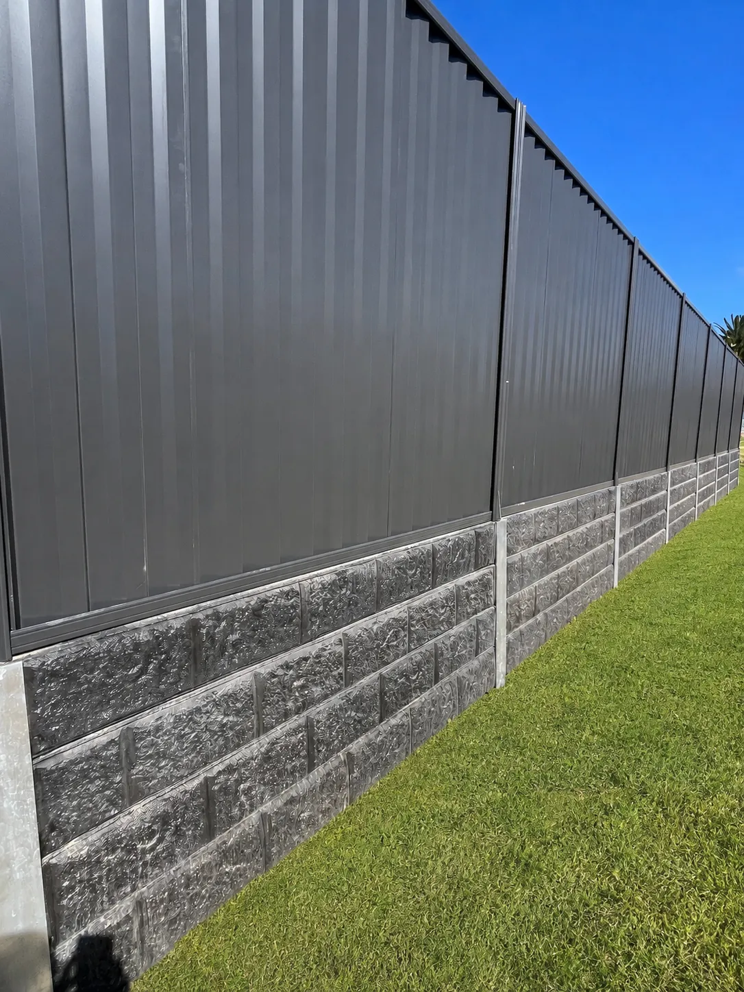 Close view of a charcoal metal fence above dark block-pattern concrete sleepers