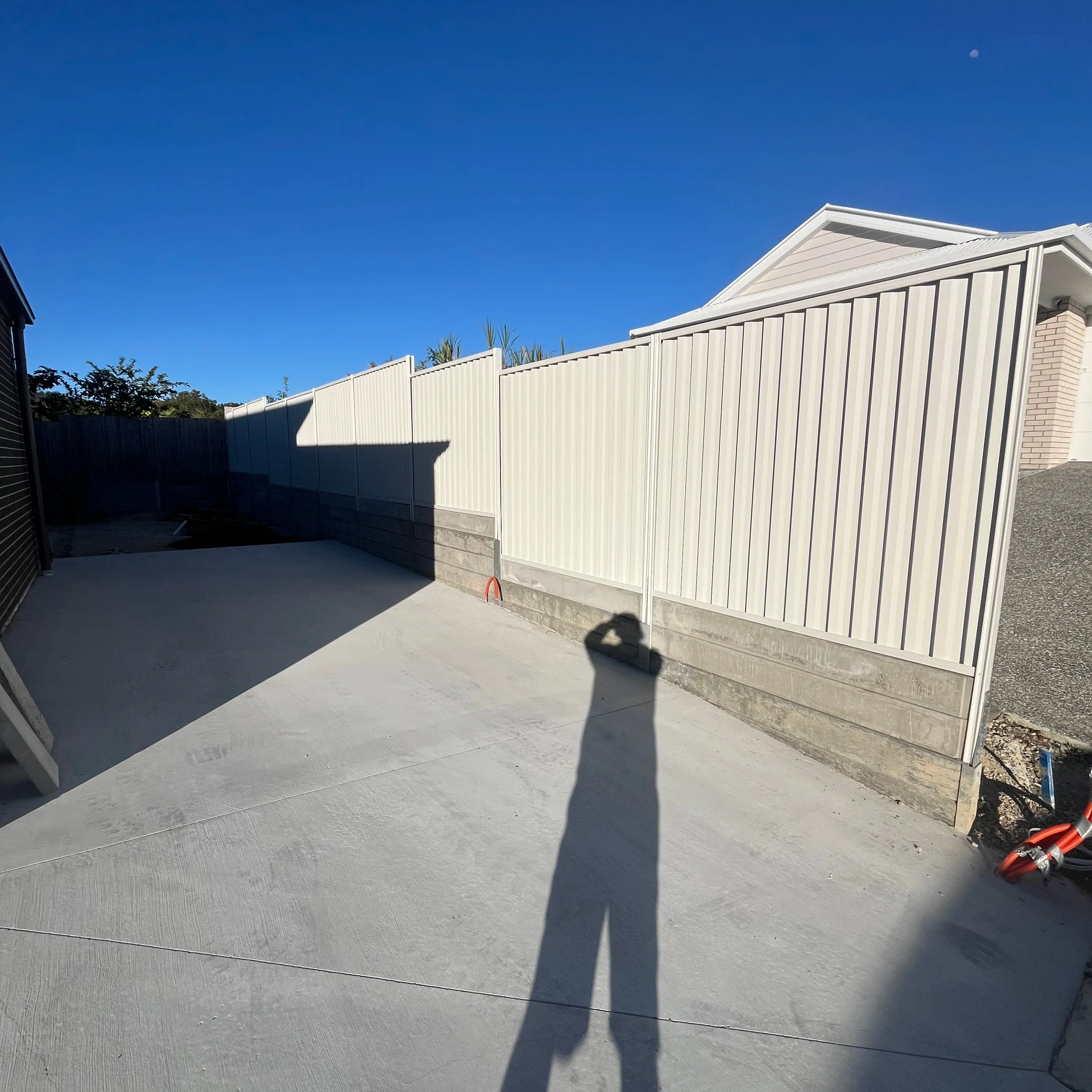 Cream metal boundary fence running alongside a concrete driveway