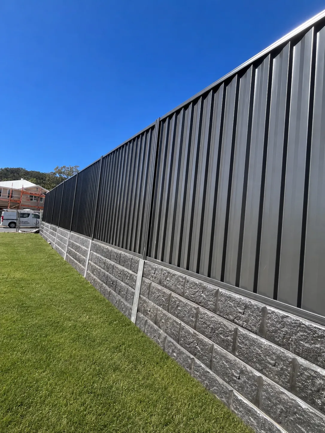 Long charcoal metal boundary fence mounted above a concrete sleeper retaining wall