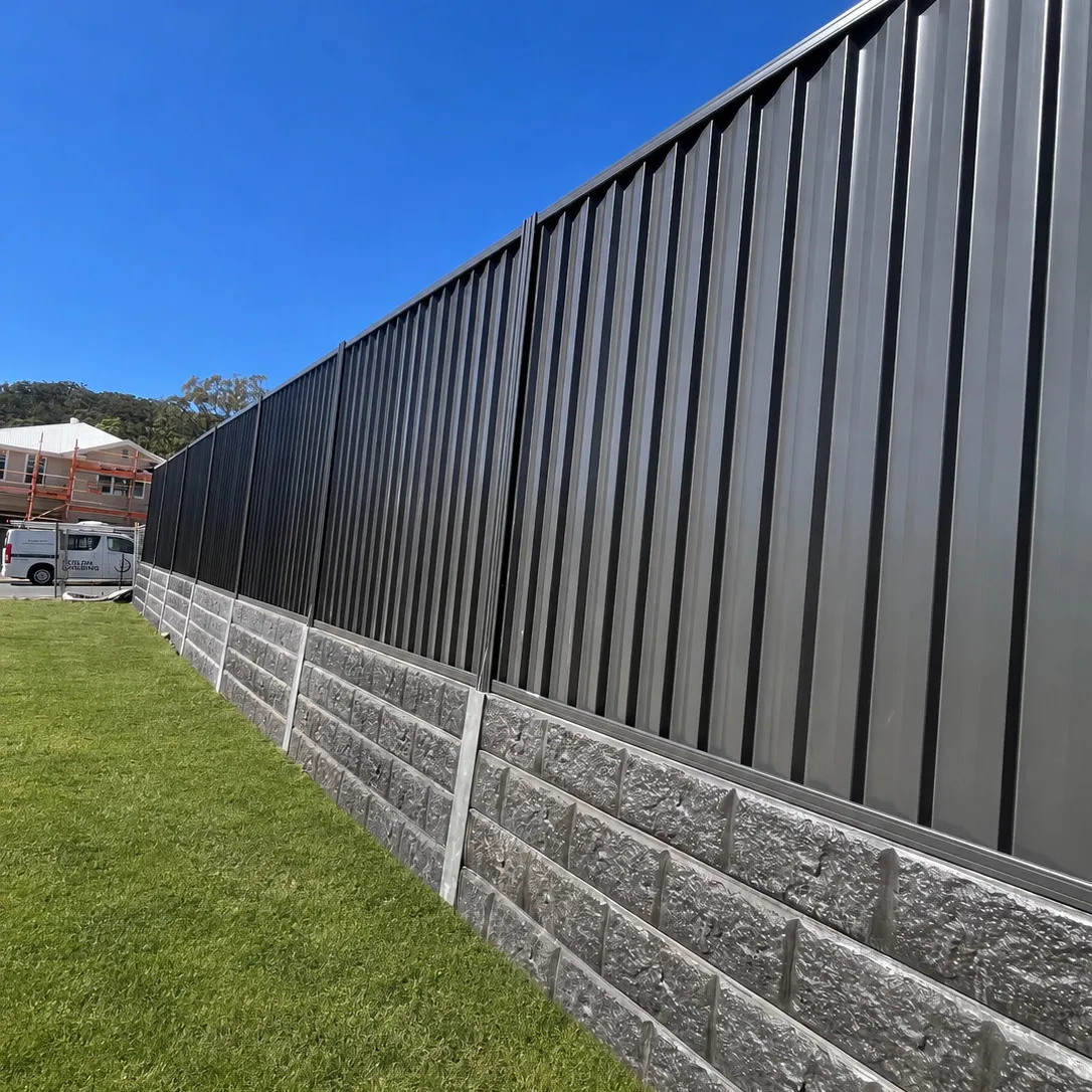 Long charcoal metal boundary fence mounted above a concrete sleeper retaining wall