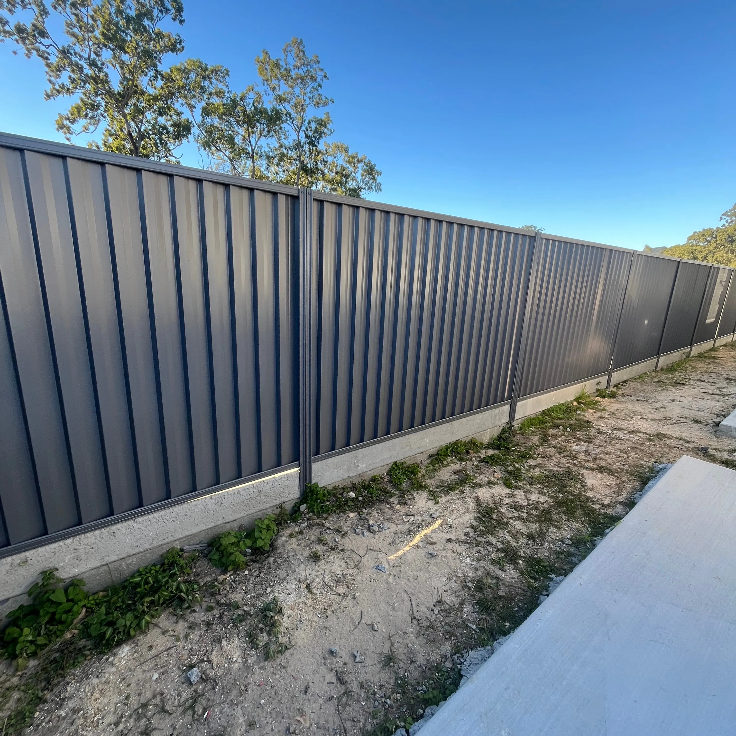 Long charcoal metal boundary fence mounted above concrete sleepers