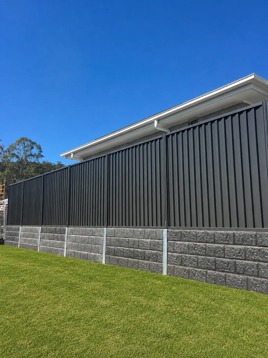 Charcoal metal boundary fence and concrete sleeper retaining wall beside a new home