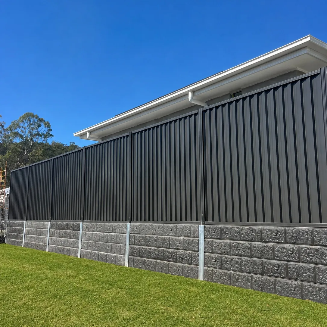 Charcoal metal boundary fence and concrete sleeper retaining wall beside a new home