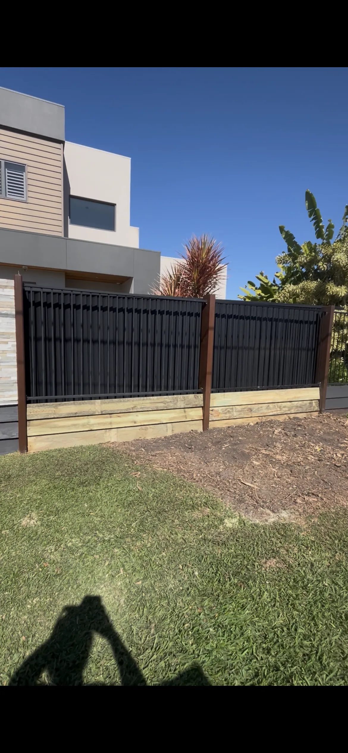 Black vertical-slat fence above a timber retaining wall