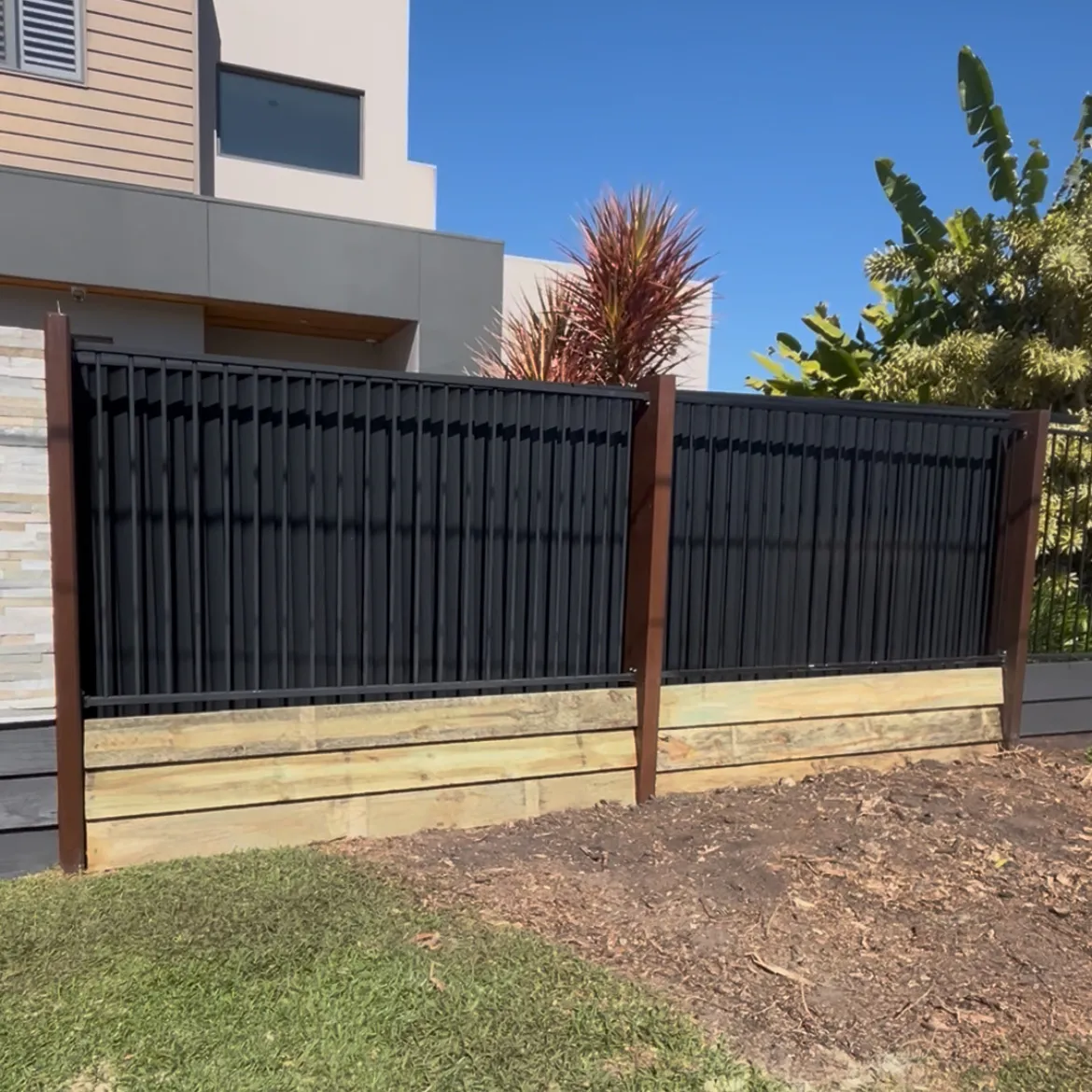 Black vertical-slat fence above a timber retaining wall